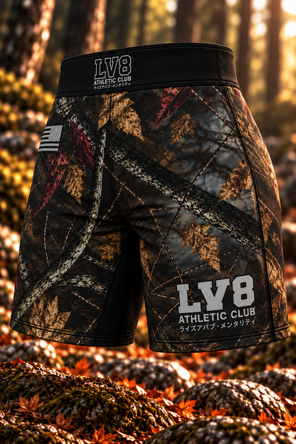 Angled front view of women's LV8 Woods shorts with woodland camouflage, a black waistband, gray LV8 branding, and monochrome American flag.